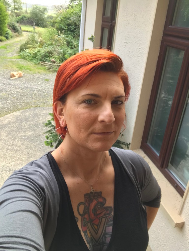 A photo of Veronica from late 2018. Her hair is dyed auburn, she's wearing a v-necked top and a duster, and she has fairly light makeup.